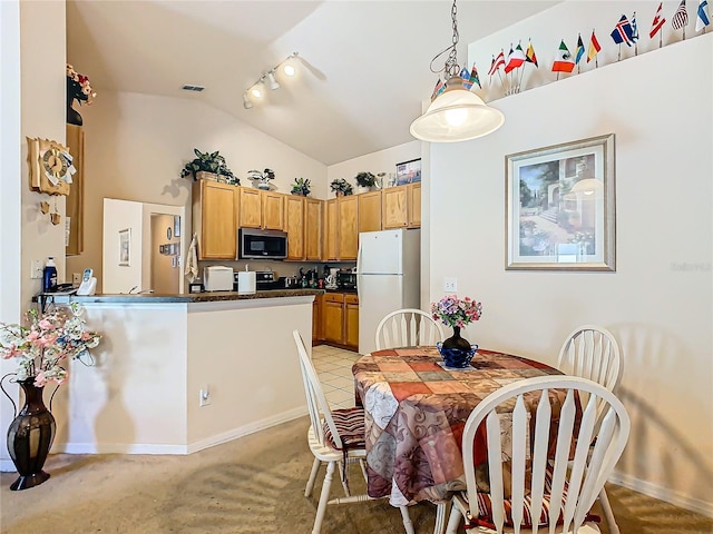 dining room with track lighting, vaulted ceiling, and light carpet