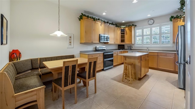 kitchen with light brown cabinetry, light tile patterned flooring, a center island, stainless steel appliances, and decorative light fixtures