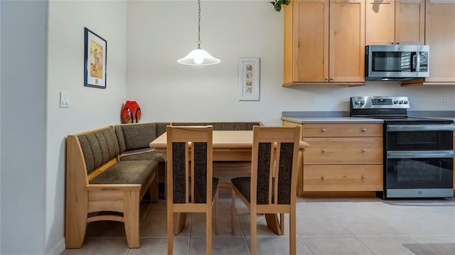 kitchen featuring appliances with stainless steel finishes, light brown cabinetry, hanging light fixtures, and light tile patterned floors