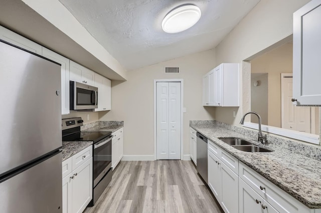 kitchen with white cabinetry, sink, appliances with stainless steel finishes, light hardwood / wood-style flooring, and vaulted ceiling