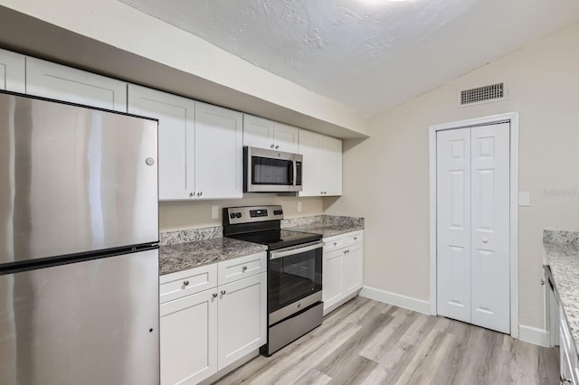 kitchen with white cabinetry, appliances with stainless steel finishes, stone counters, vaulted ceiling, and light hardwood / wood-style flooring