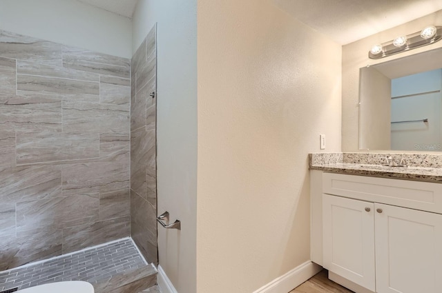 bathroom with toilet, vanity, hardwood / wood-style floors, and a tile shower