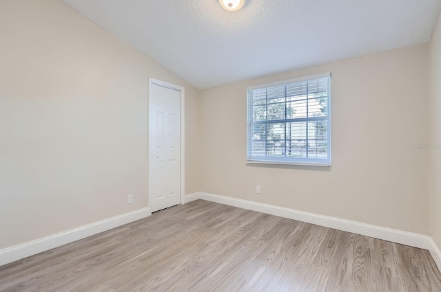 empty room with a textured ceiling, light wood-type flooring, and lofted ceiling