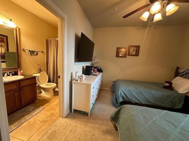 bedroom featuring ensuite bath, sink, light tile patterned floors, and ceiling fan