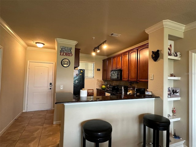 kitchen with black appliances, a kitchen bar, kitchen peninsula, tile patterned floors, and crown molding