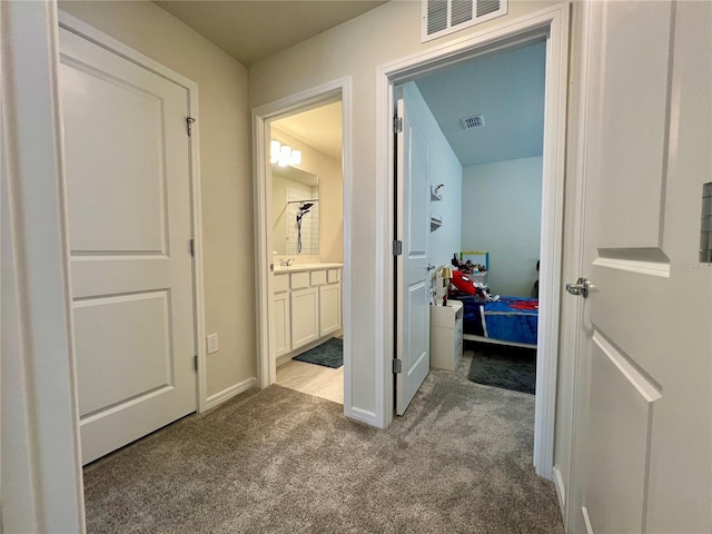 hall with carpet floors, visible vents, a sink, and baseboards