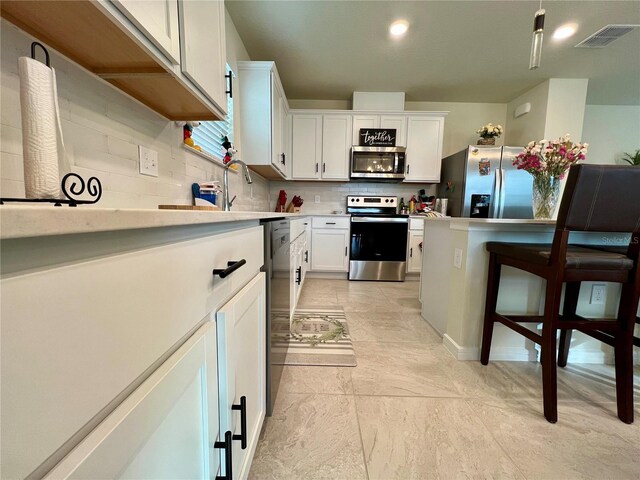 kitchen with stainless steel appliances, a breakfast bar, visible vents, white cabinets, and light countertops