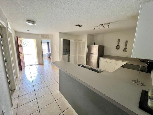 kitchen featuring sink, stainless steel fridge, a textured ceiling, white cabinets, and light tile patterned flooring