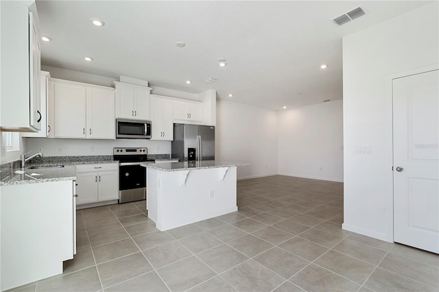 kitchen with appliances with stainless steel finishes, sink, a center island, white cabinets, and light stone counters