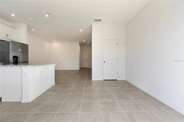 kitchen featuring light stone countertops, light tile patterned flooring, a kitchen breakfast bar, white cabinetry, and stainless steel fridge with ice dispenser