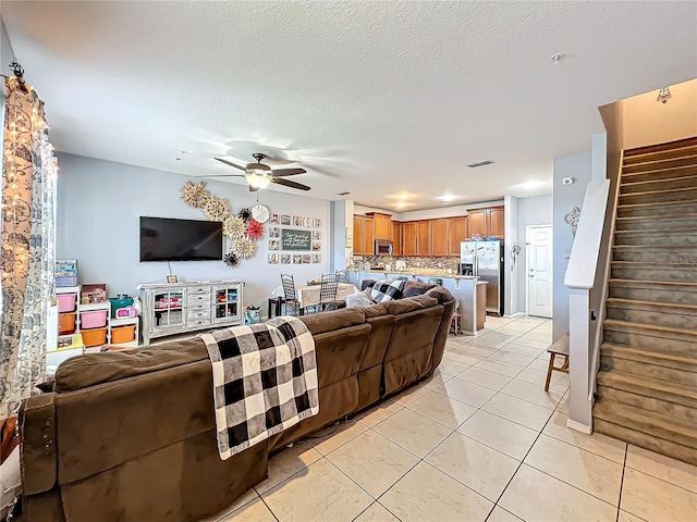 living room featuring a textured ceiling, light tile patterned floors, and ceiling fan