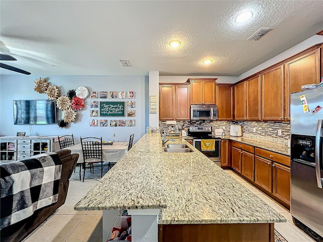 kitchen featuring stainless steel appliances, light stone countertops, and an island with sink