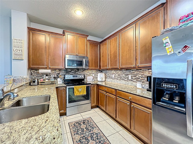 kitchen featuring appliances with stainless steel finishes, sink, a textured ceiling, light stone counters, and decorative backsplash