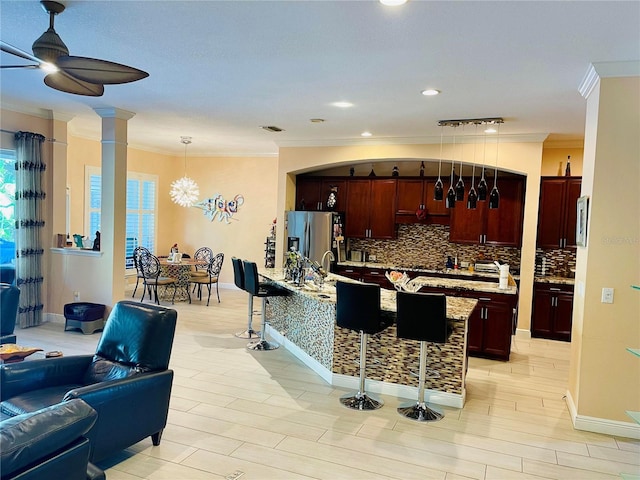 kitchen featuring hanging light fixtures, tasteful backsplash, stainless steel fridge, a breakfast bar area, and ornamental molding