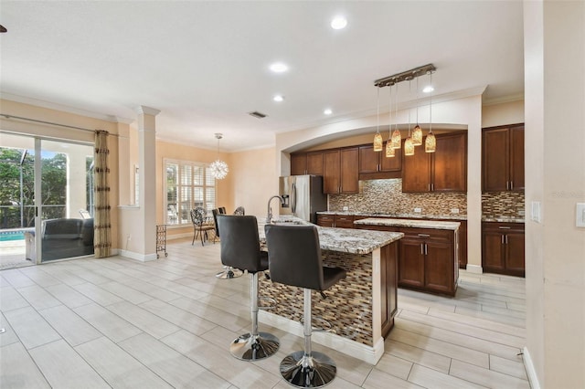 kitchen featuring light stone counters, decorative light fixtures, a center island with sink, and stainless steel fridge with ice dispenser