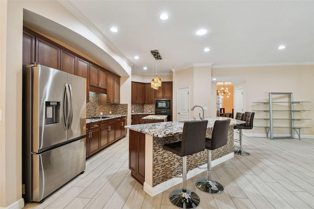 kitchen with an island with sink, hanging light fixtures, light stone countertops, black appliances, and a kitchen bar