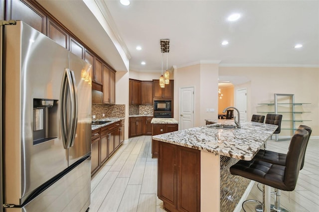 kitchen with black microwave, a sink, hanging light fixtures, stainless steel fridge with ice dispenser, and a center island with sink