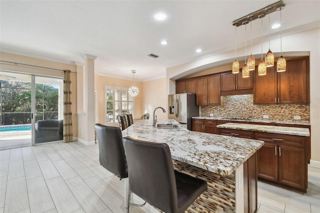 kitchen featuring pendant lighting, backsplash, a sink, an island with sink, and stainless steel fridge with ice dispenser