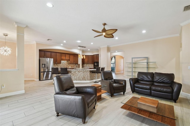 living room featuring arched walkways, crown molding, light wood-style floors, baseboards, and ceiling fan with notable chandelier