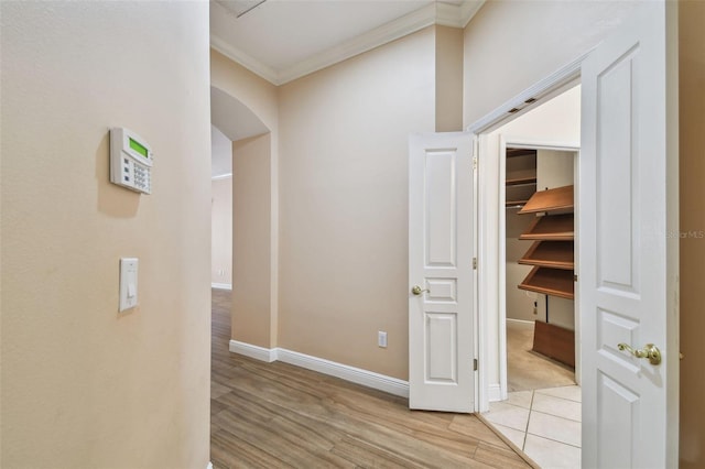 hall featuring ornamental molding, arched walkways, baseboards, and light wood finished floors