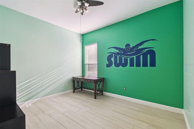 unfurnished room with an accent wall, light wood-style flooring, a ceiling fan, and baseboards