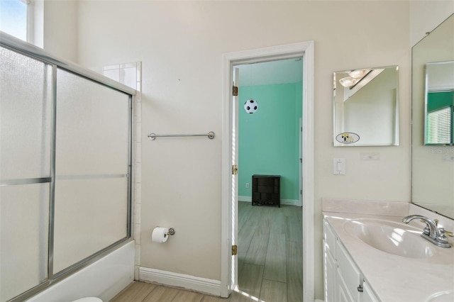 bathroom with baseboards, toilet, shower / bath combination with glass door, wood finished floors, and vanity