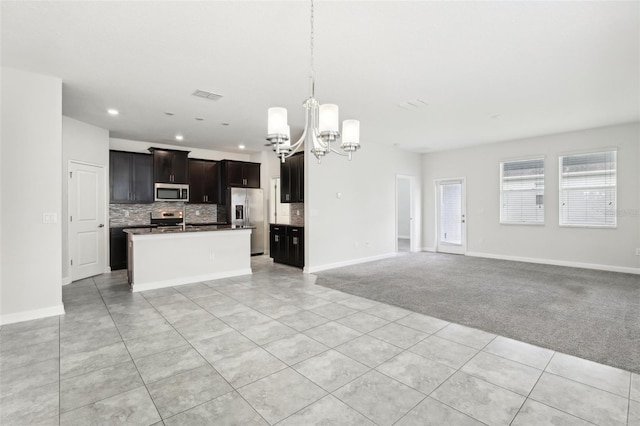 kitchen featuring light carpet, appliances with stainless steel finishes, a kitchen island with sink, pendant lighting, and an inviting chandelier