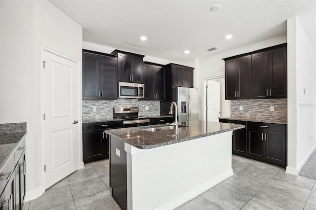 kitchen featuring backsplash, a kitchen island with sink, sink, a textured ceiling, and appliances with stainless steel finishes