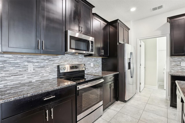 kitchen with decorative backsplash, light tile patterned floors, stainless steel appliances, and dark stone counters