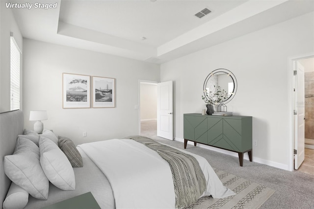 bedroom with light carpet, a tray ceiling, and ensuite bath