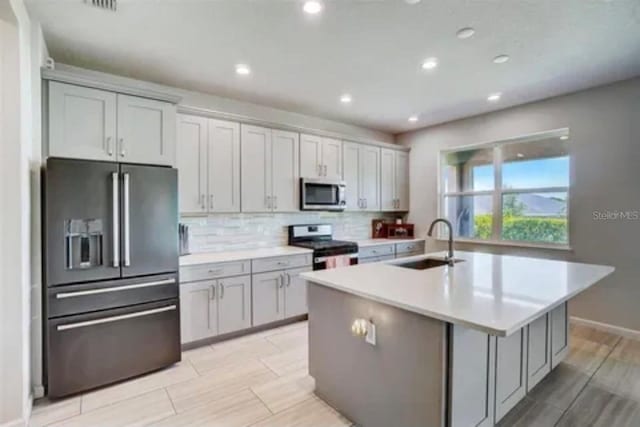 kitchen with tasteful backsplash, a kitchen island with sink, sink, gray cabinets, and stainless steel appliances