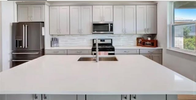 kitchen with a center island with sink, appliances with stainless steel finishes, gray cabinetry, and backsplash