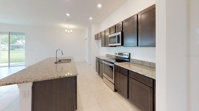 kitchen with a center island with sink, stainless steel appliances, sink, dark brown cabinetry, and light stone counters