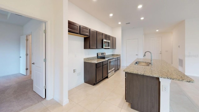 kitchen with sink, stainless steel appliances, light stone counters, light colored carpet, and a kitchen island with sink