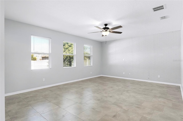 tiled spare room with ceiling fan, brick wall, and a textured ceiling