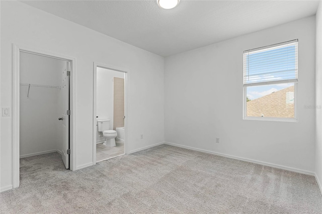 unfurnished bedroom with light carpet, a textured ceiling, a spacious closet, connected bathroom, and a closet