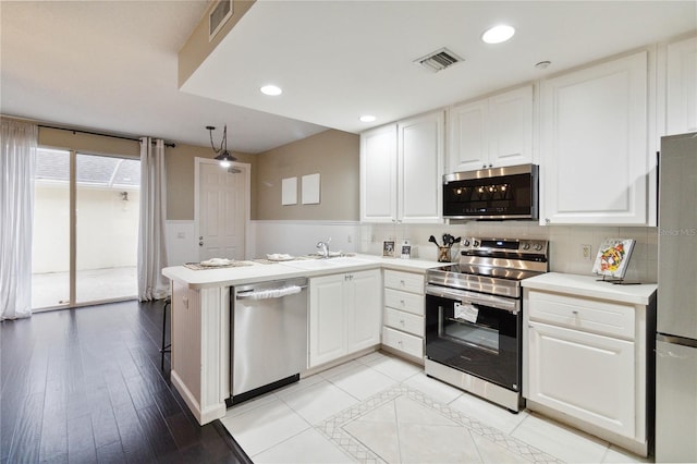 kitchen with kitchen peninsula, backsplash, white cabinetry, light wood-type flooring, and stainless steel appliances