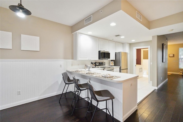 kitchen featuring dark hardwood / wood-style flooring, kitchen peninsula, a kitchen breakfast bar, white cabinetry, and stainless steel appliances