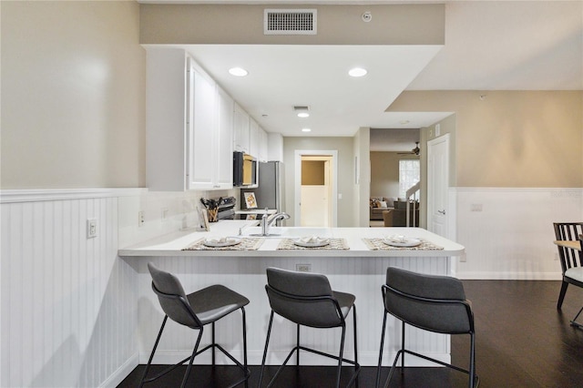 kitchen featuring kitchen peninsula, white cabinets, a breakfast bar area, dark wood-type flooring, and stainless steel appliances