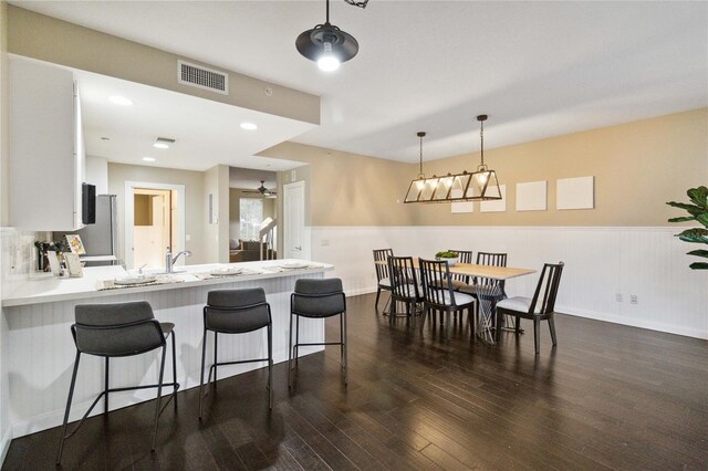 kitchen featuring kitchen peninsula, white cabinets, ceiling fan, a kitchen breakfast bar, and dark hardwood / wood-style floors