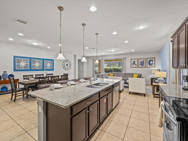 8832 Macapa Dr, Kissimmee, FL 34747 - kitchen featuring a sink, appliances with stainless steel finishes, dark brown cabinets, a center island with sink, and light tile patterned floors
