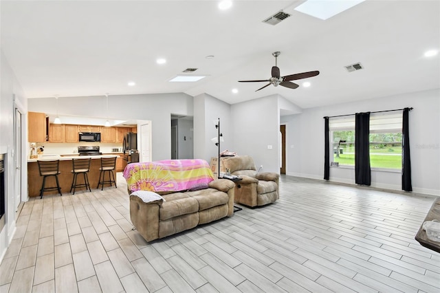 living room with vaulted ceiling with skylight, light wood-type flooring, and ceiling fan