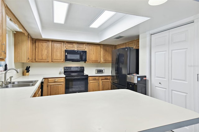 kitchen featuring kitchen peninsula, a tray ceiling, black appliances, and sink