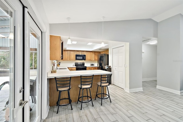 kitchen with black appliances, a sink, a peninsula, light countertops, and lofted ceiling