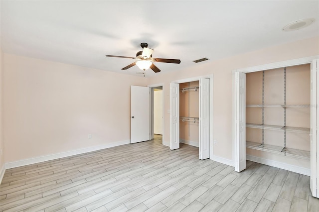 unfurnished bedroom featuring baseboards, visible vents, ceiling fan, light wood-type flooring, and two closets