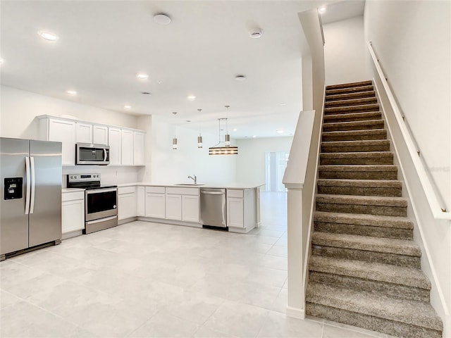 kitchen with white cabinets, appliances with stainless steel finishes, kitchen peninsula, and hanging light fixtures