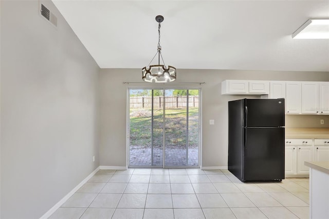 kitchen with light tile patterned floors, an inviting chandelier, white cabinetry, black refrigerator, and pendant lighting