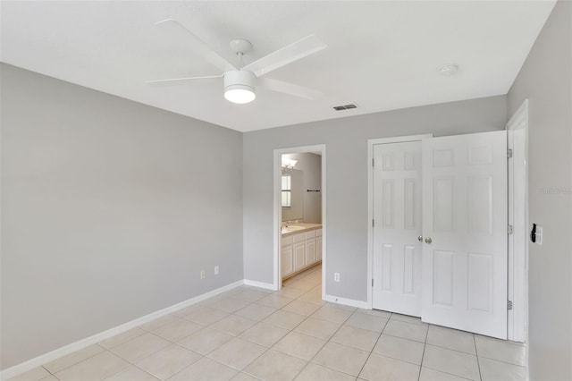 unfurnished bedroom with a closet, ensuite bath, light tile patterned floors, and ceiling fan