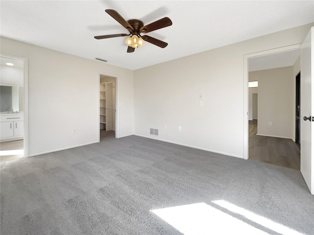 interior space featuring ceiling fan, a spacious closet, ensuite bathroom, dark colored carpet, and a closet