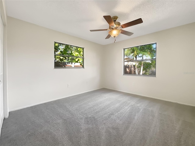 spare room featuring ceiling fan, a textured ceiling, plenty of natural light, and dark colored carpet